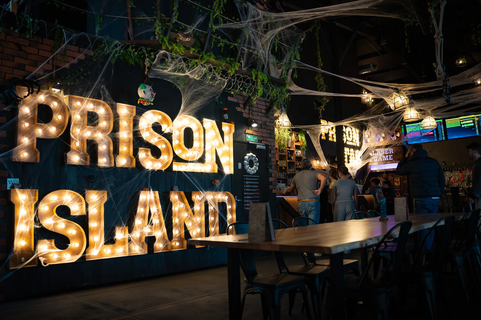 Le bar sous l'enseigne lumineuse Prison Island, tables en bois au premier plan