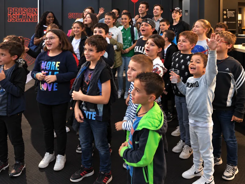 Un groupe d'enfants d'une association, debout dans la salle, lève la main en souriant