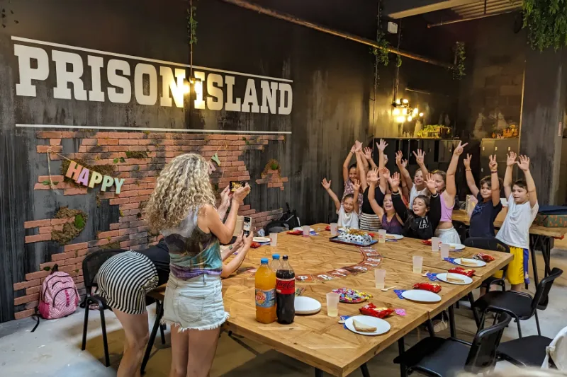 Une table d'anniversaire sous le mur Prison Island, les enfants lèvent les bras